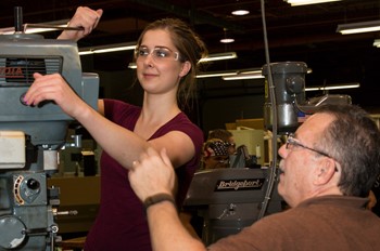 Student working on a machine with assistance from her instructor.