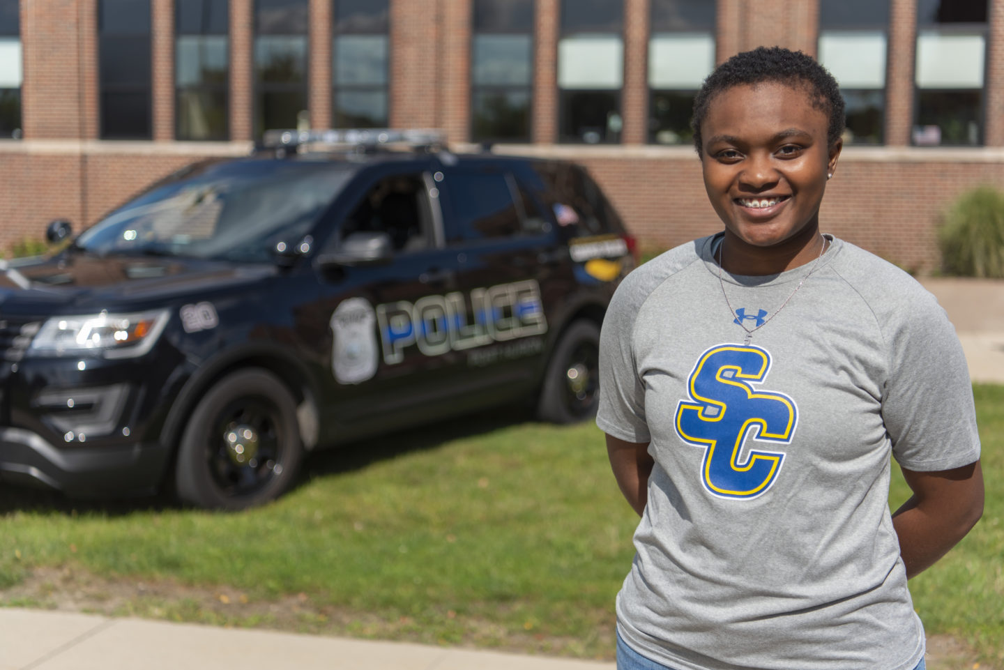 Female criminal justice student poses for photo in front of police car on campus