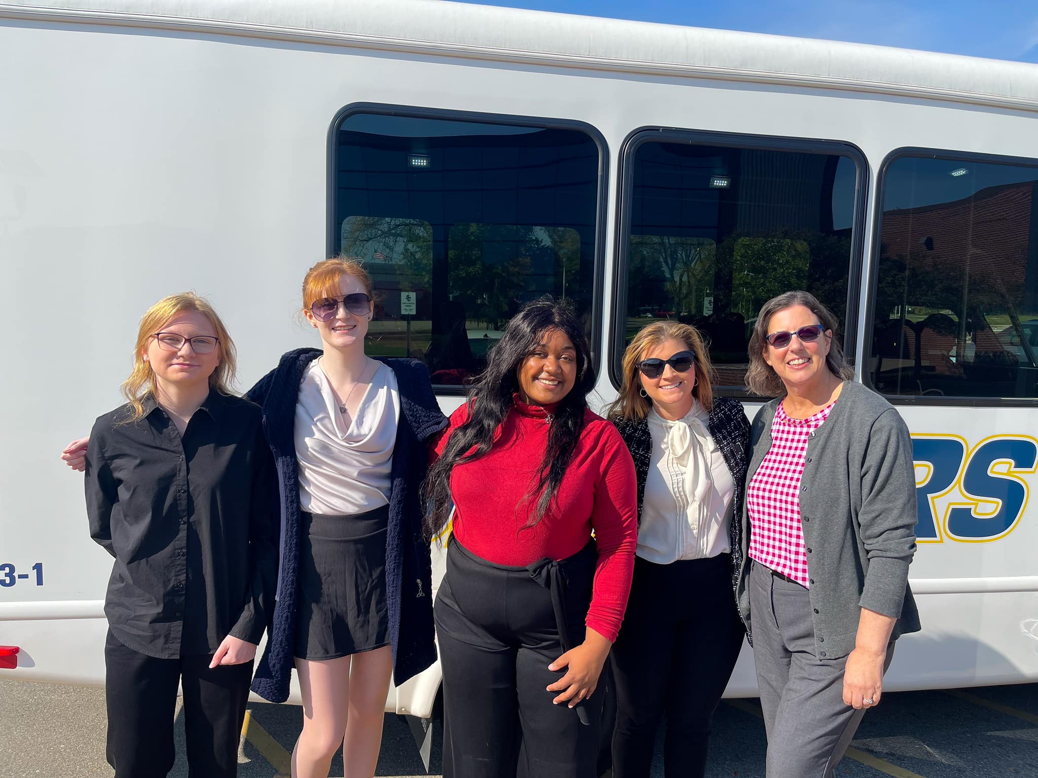 students standing with faculty in front of the skippers bus